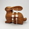 Pearl earrings hanging from a wooden rabbit-shaped holder on a white background