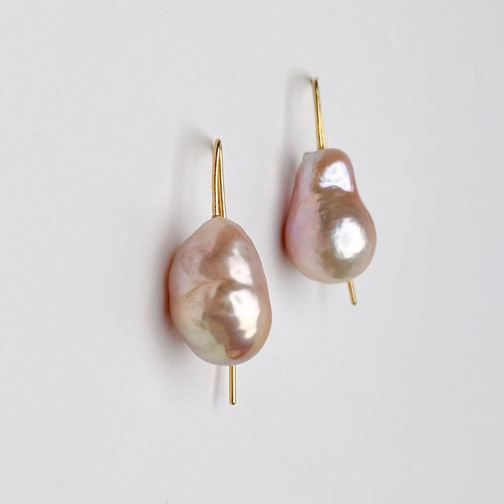 Pair of pearl earrings with gold hooks on a light gray background