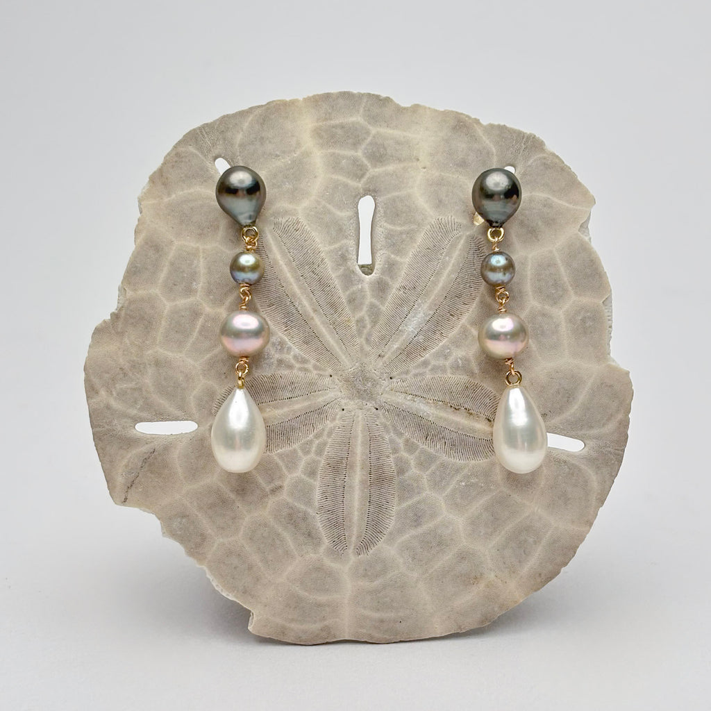 Four tiered earrings with different color pearls displayed on a sand dollar with a gray background