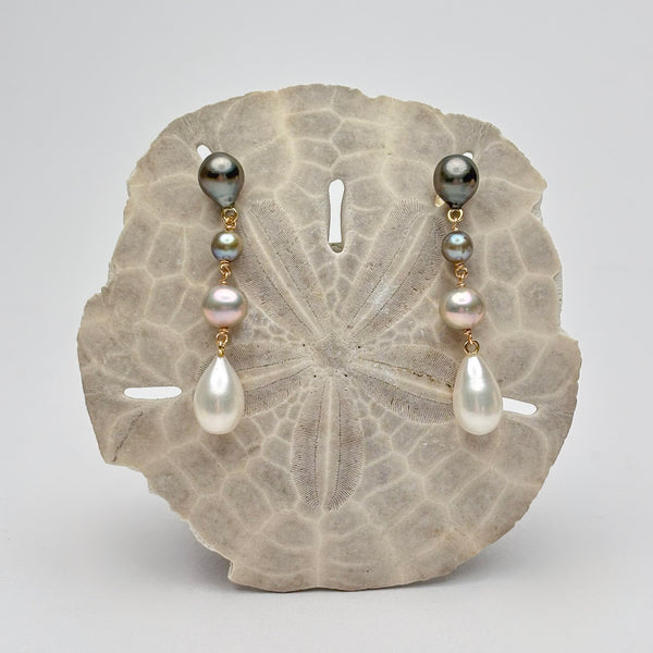 Four tiered earrings with different color pearls displayed on a sand dollar with a gray background