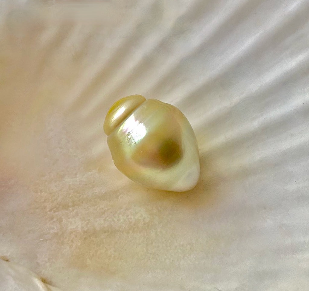 A large, light golden yellow South Sea pearl with a baroque, banded drop shape, placed on a white surface.