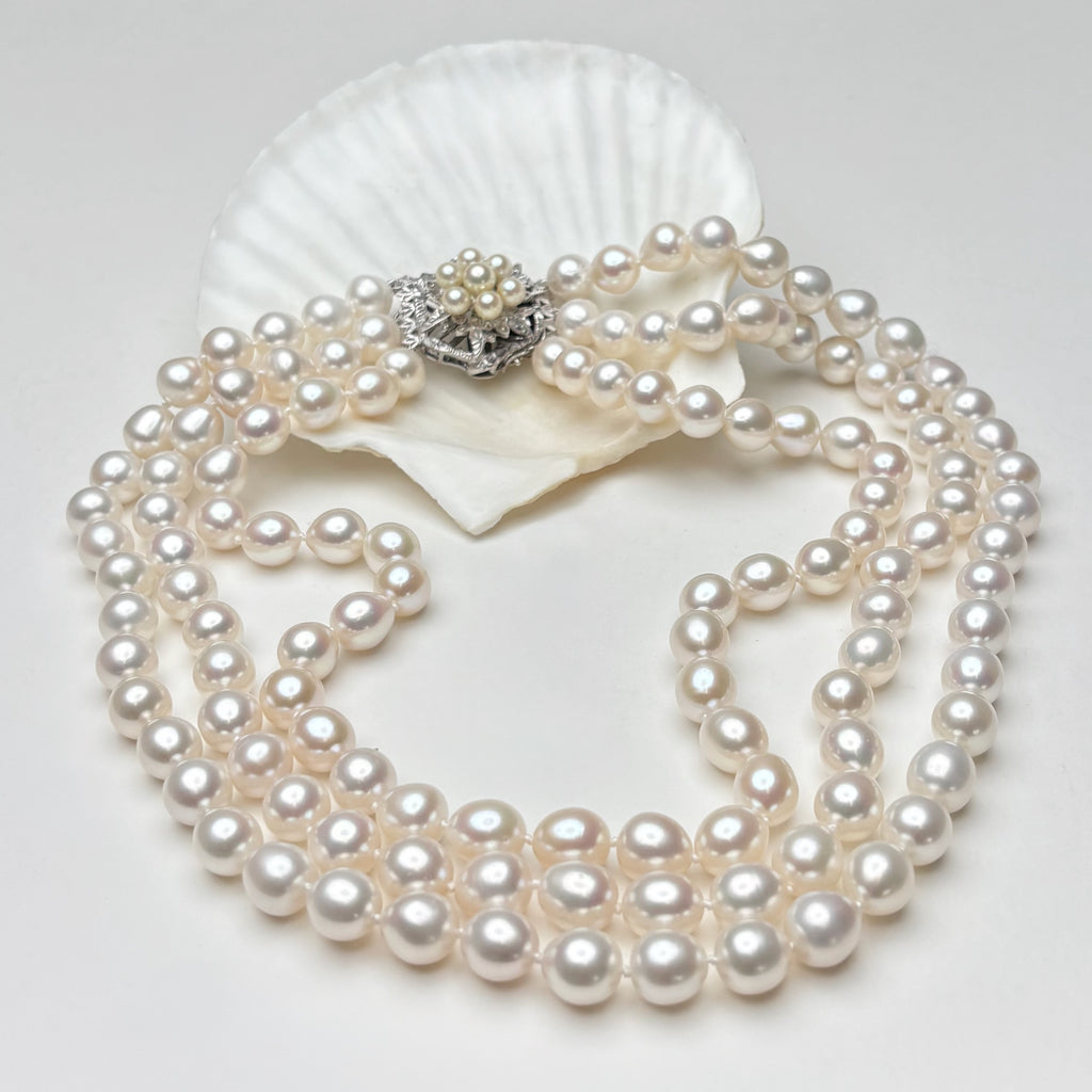 Pearl necklace with a vintage white gold clasp on a white shell against a light gray background