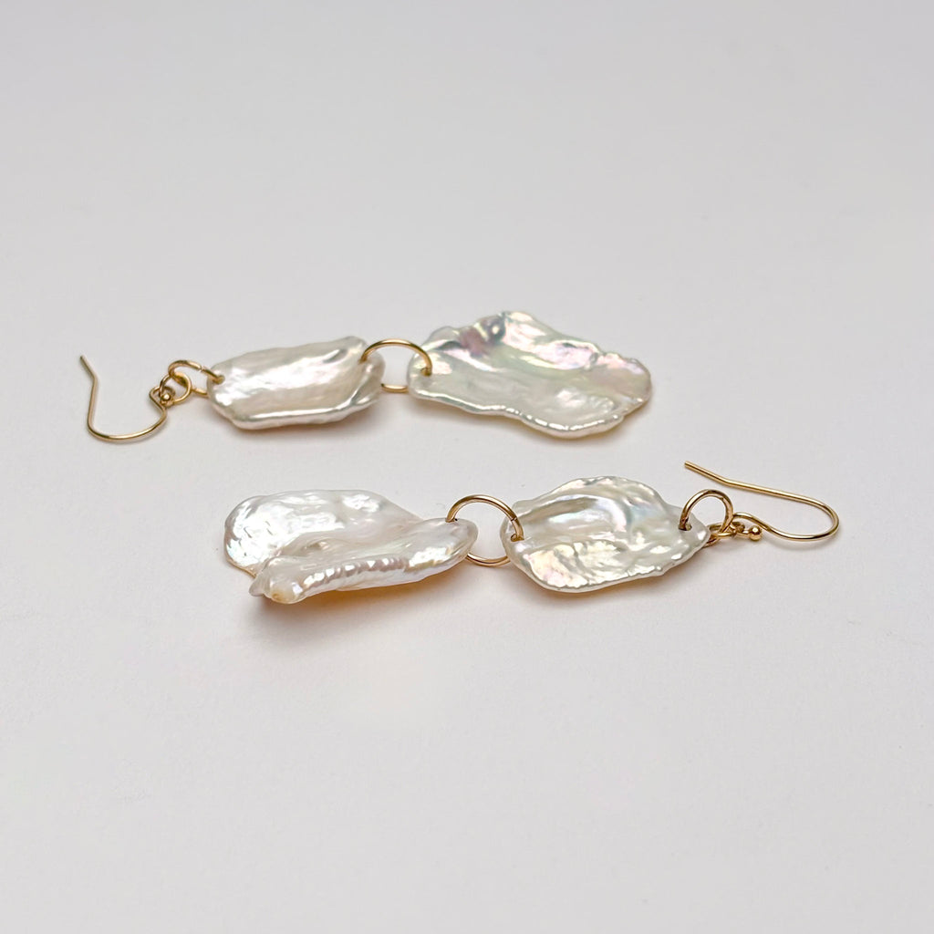 Pair of petal pearl earrings with gold hooks on a light gray background
