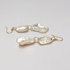 Pair of petal pearl earrings with gold hooks on a light gray background